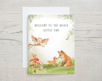 Greeting card with forest animals and 'Welcome to the World Little One' text on a wooden surface.