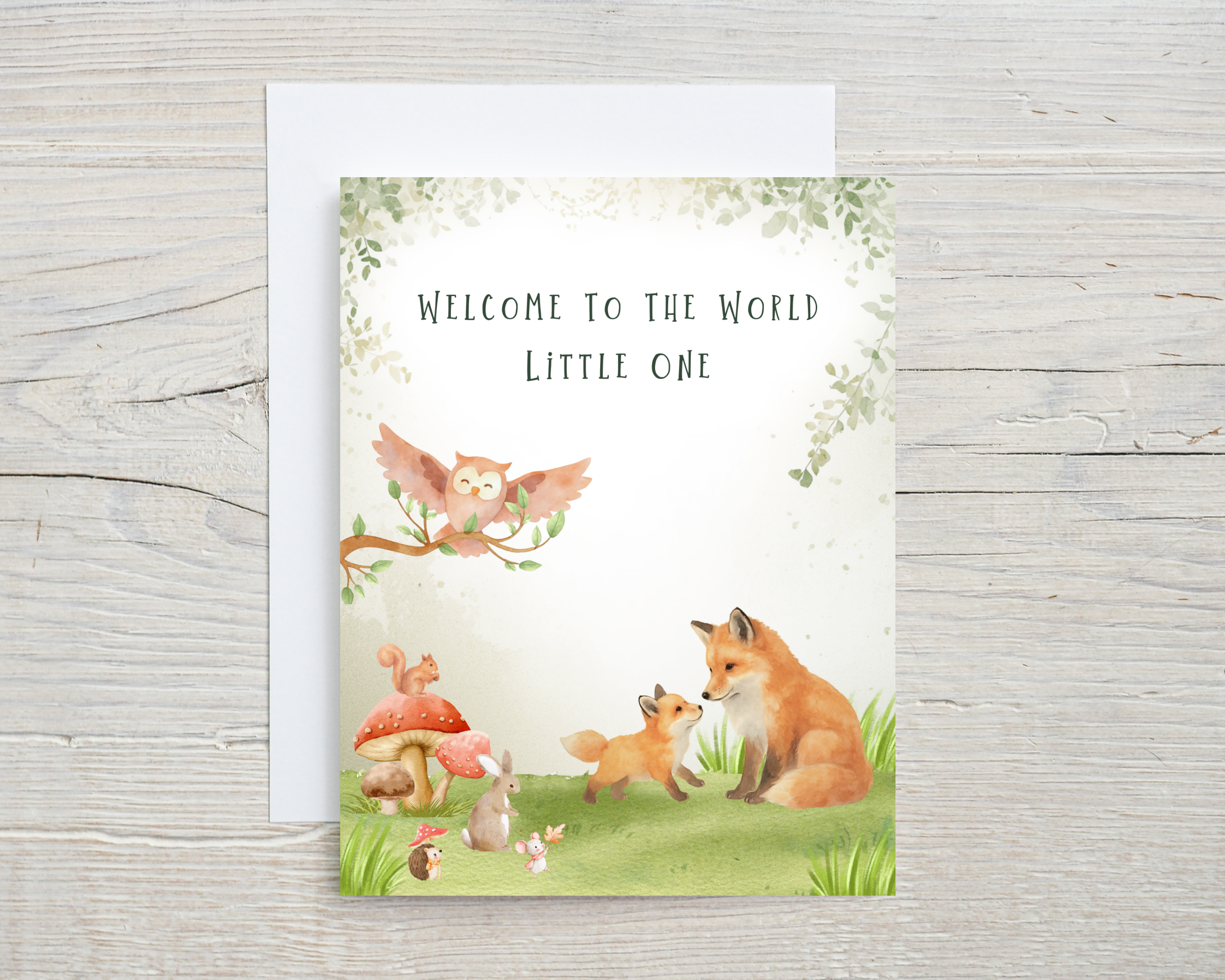 Greeting card with forest animals and 'Welcome to the World Little One' text on a wooden surface.