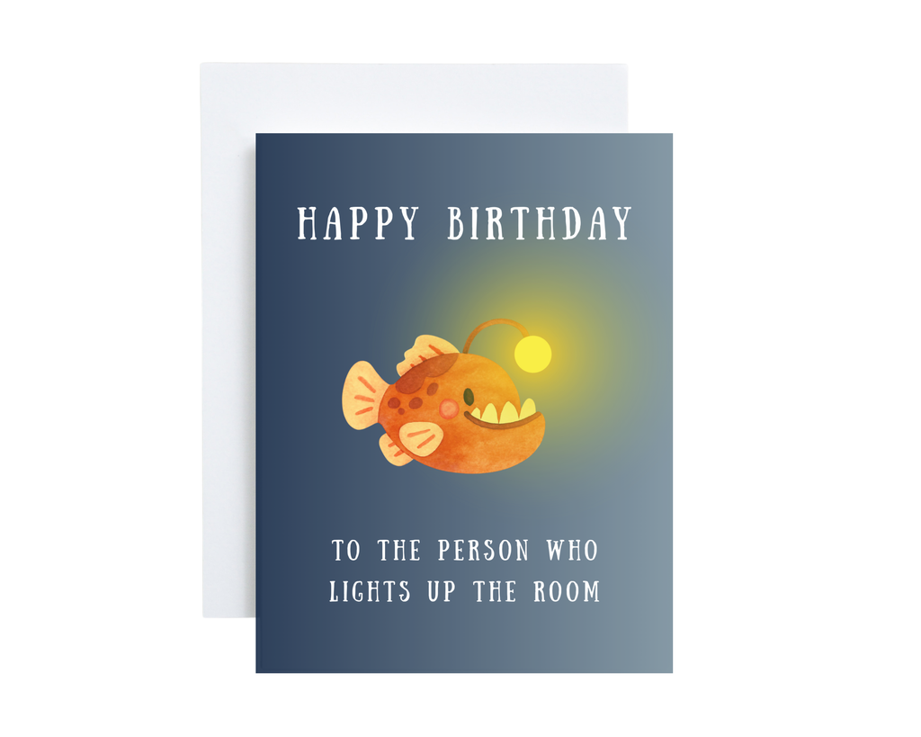 Birthday card with a cartoon angler fish and humorous text "Happy Birthday To The Person Who Lights Up The Room" on a blue background